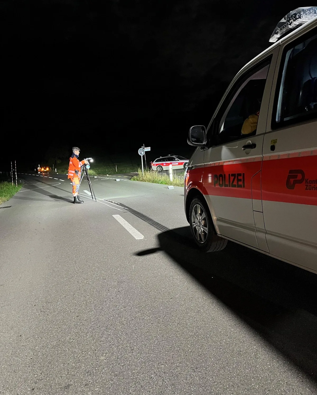 Man sieht eine Unfallstelle in der Nacht. Auf dem Bild sind ein Polizeiauto und Polizisten bei der Unfallaufnahme zu sehen.